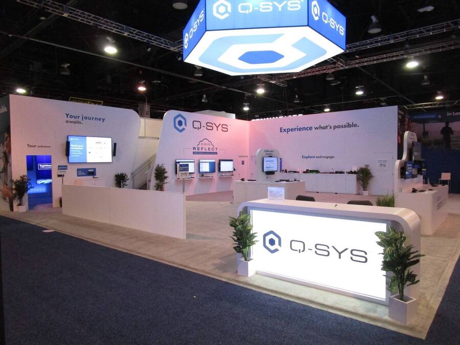 Q-SYS 60x60 double-deck island at InfoComm 2024 with a hexagon hanging sign