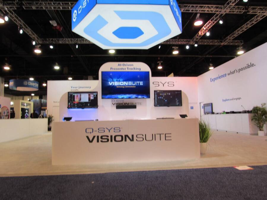 Q-SYS VisionSuite demo counter under a lit hexagon sign at InfoComm 2024